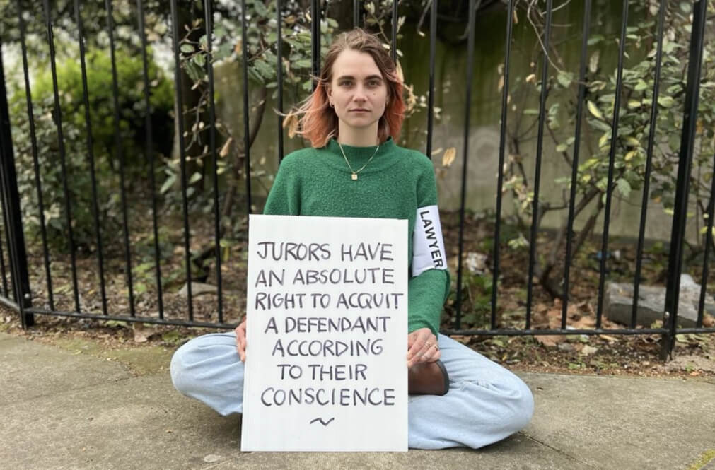 Laura Korte sits cross legged holding a sign reading 'Jurors have an absolute right to acquit a defendant according to their conscience'